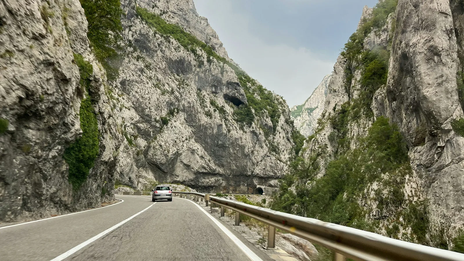 Un'auto sulla strada del canyon, guardrail da un lato e roccia dall'altro